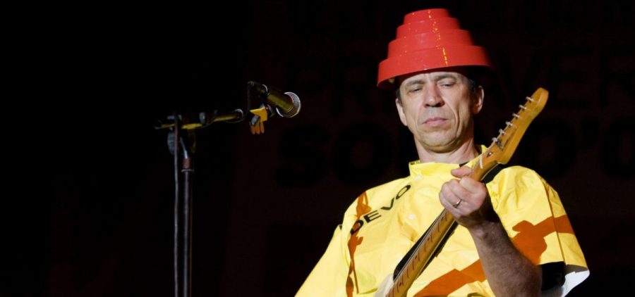 Devo guitarist Bob Mothersbaugh performs on stage wearing a yellow outfit and a red flowerpot looking thing on his head.
