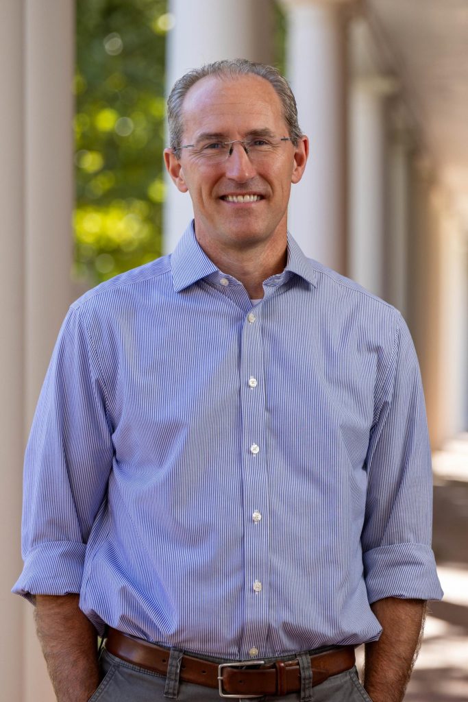A man wearing glasses and a button up shirt poses outside for a portrait.