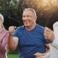 Senior man, fitness and group in garden at retirement village, health and exercise class in morning. People, happy and workout with diversity, excited and training with cardio in summer for wellness