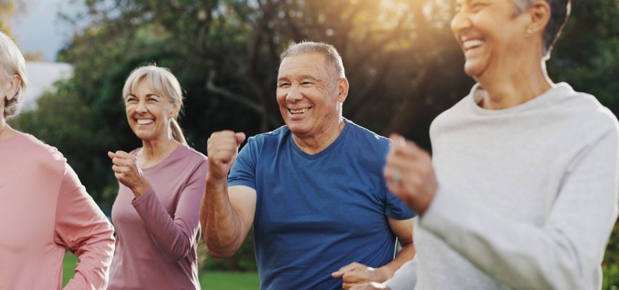 Senior man, fitness and group in garden at retirement village, health and exercise class in morning. People, happy and workout with diversity, excited and training with cardio in summer for wellness