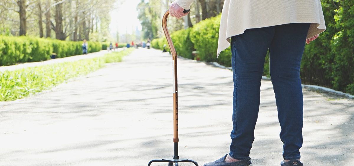 An elderly person walks with a cane in a paved path in a park