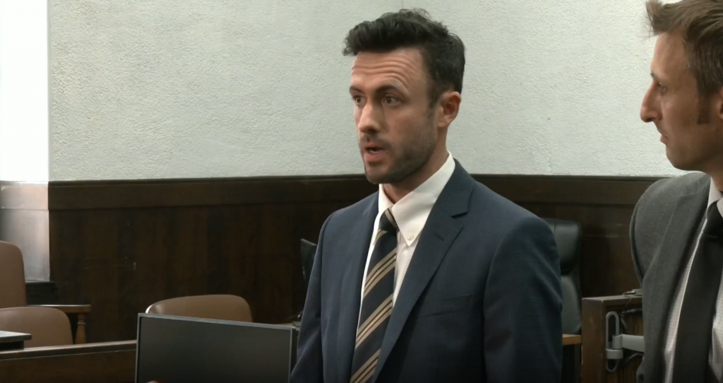 Two men in suits talk to reporters in a courtroom.