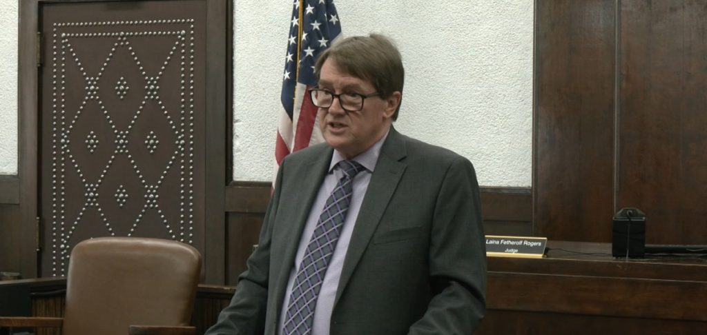 William Archer stands and talks to reporters inside of a courtroom.