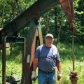 Bob Wilson stands in front of a natural gas pump in the middle of the woods.