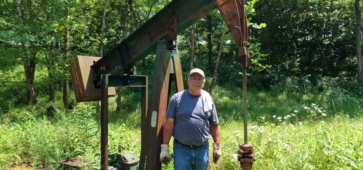 Bob Wilson stands in front of a natural gas pump in the middle of the woods.