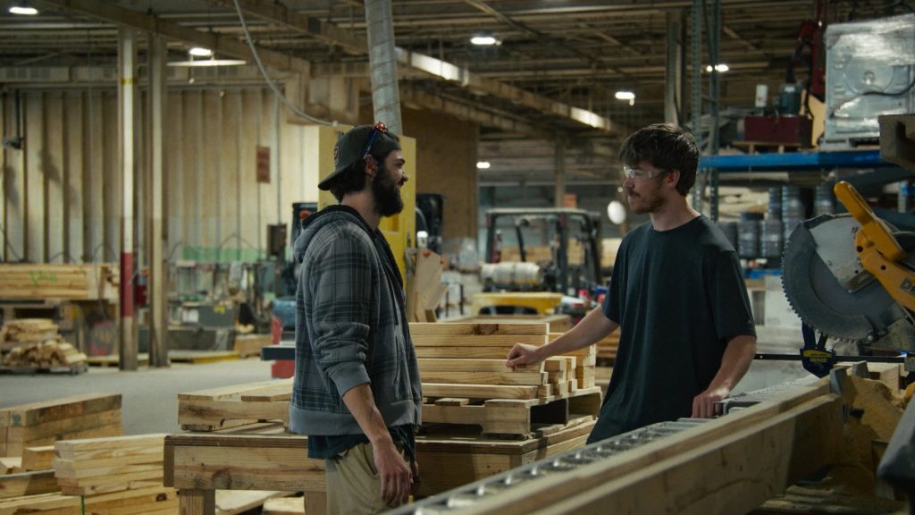 Two men stand in a lumber warehouse.