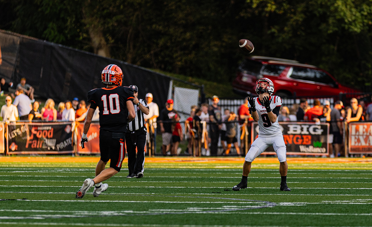 A Wheelersburg Pirate's player is running to a Jackson Ironman player while he is trying to catch the ball.