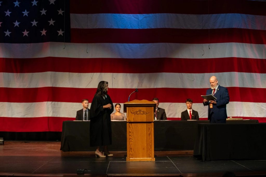 People are on state in front of an American flag for a naturalization ceremony.