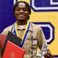 Pierra Damas Bel holds up certificates and a medal at a graduation ceremony.