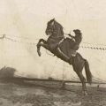 A horse rears back as Annie Oakley rides on its back in a black and white photo.