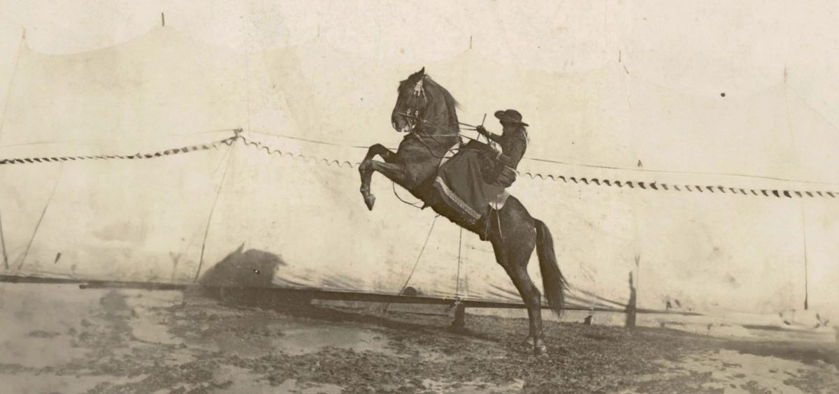 A horse rears back as Annie Oakley rides on its back in a black and white photo.