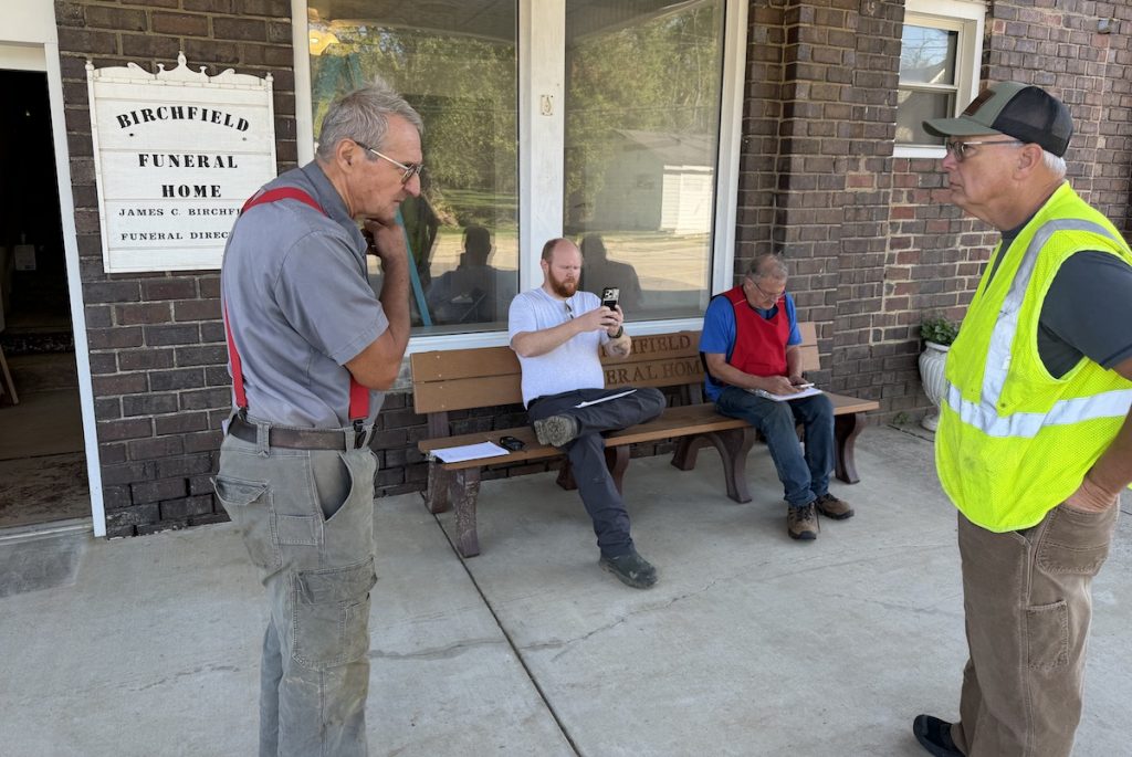 James Birchfield (left), the owner of Birchfield Funeral Home in Rutland, talks with Jeef Needs, a volunteer with the Meigs County Emergency Management Agency. On the bench, volunteers Josh Fisher (left) and Brian Taylor enter information into a phone app about the flood damage.