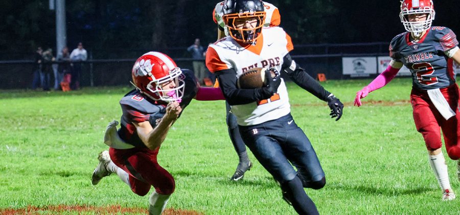 Belpre athlete is running with the ball while a Trimble player is trying to tackle him.
