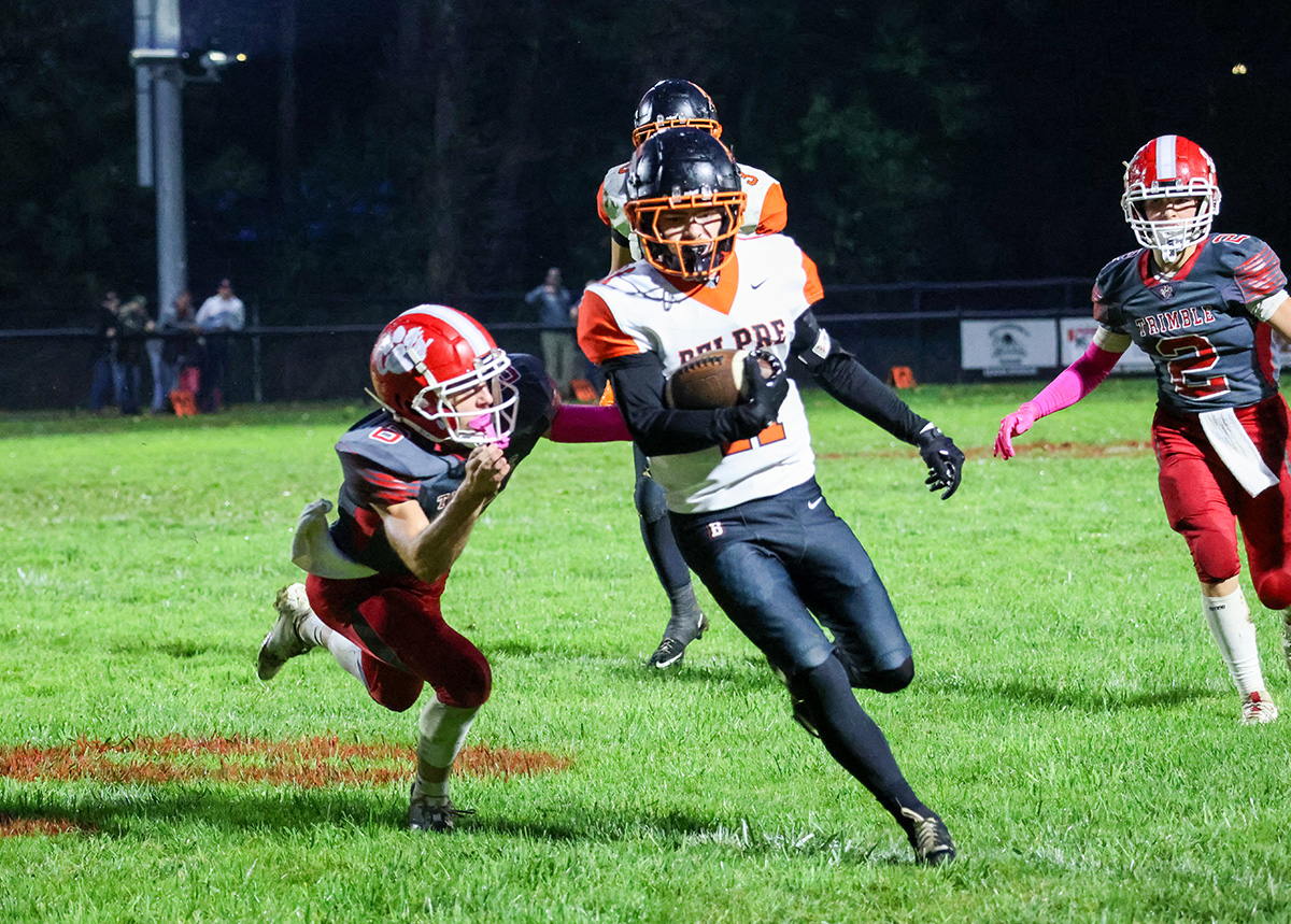Belpre athlete is running with the ball while a Trimble player is trying to tackle him.