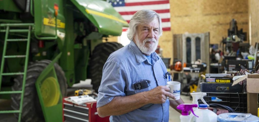 Chris Gibbs, a cattle farmer in rural Ohio, poses for a picture in his garage with a tractor in the back.