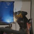 A person uses a power tool behind a blue screen.