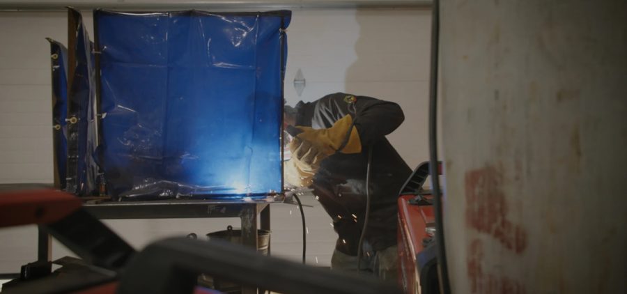 A person uses a power tool behind a blue screen.