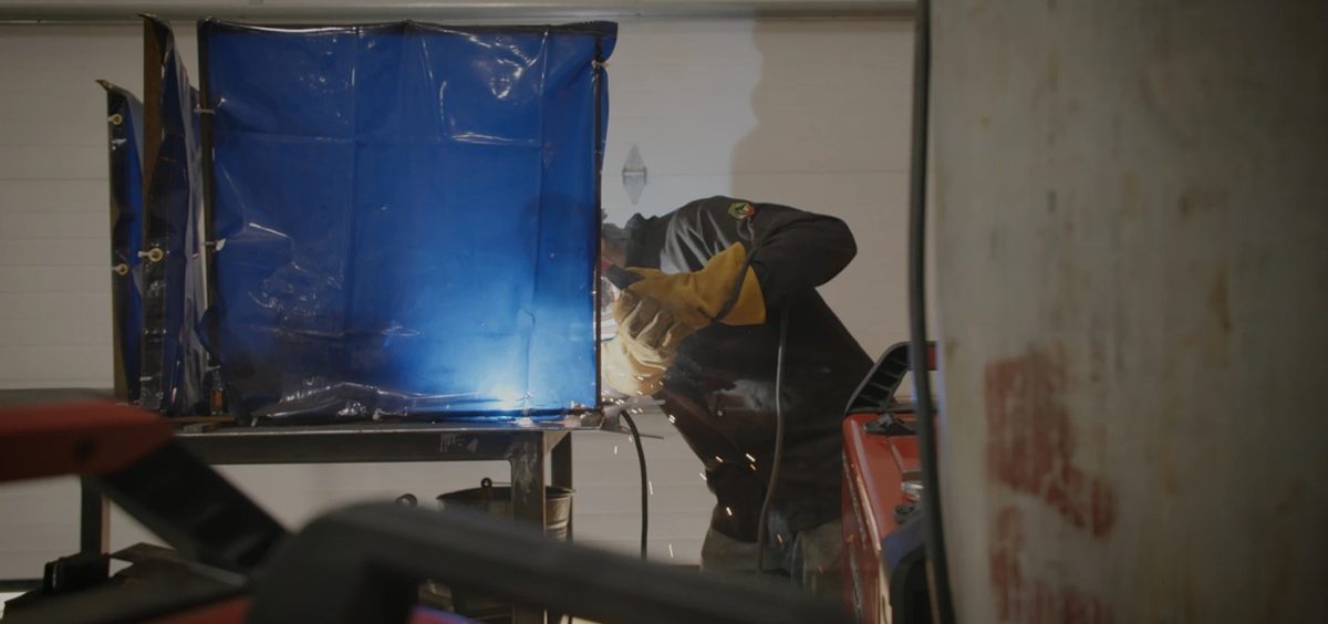 A person uses a power tool behind a blue screen.